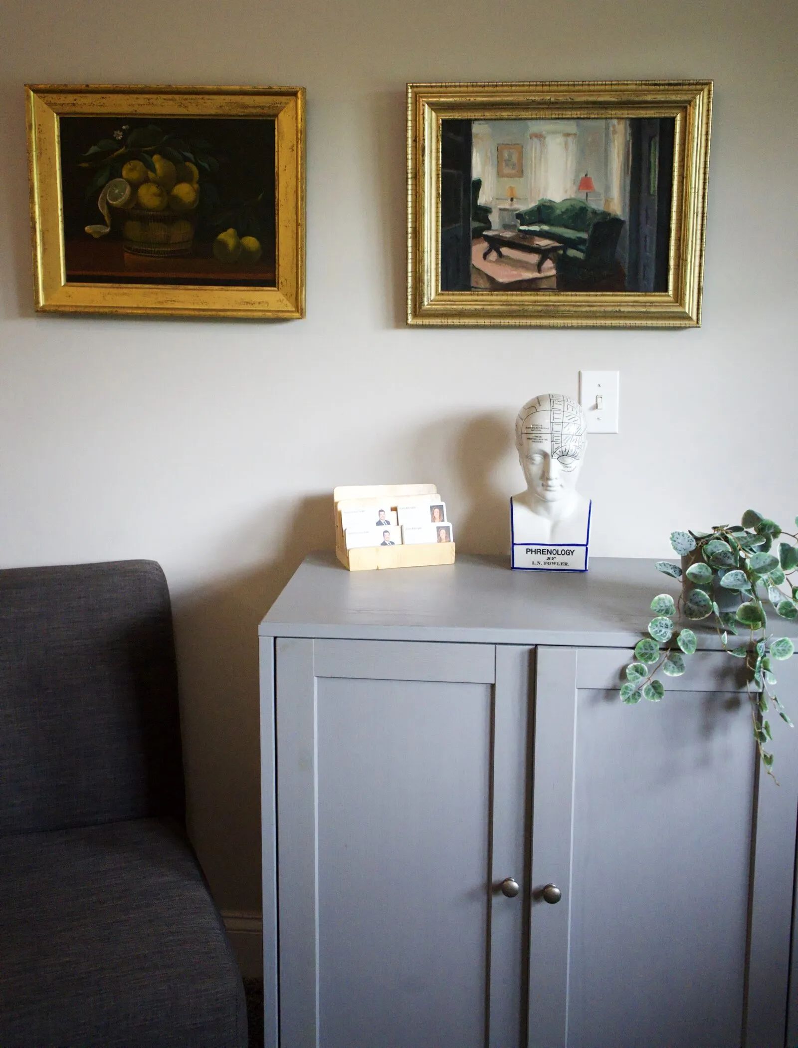 A corner of the Chadds Ford office: two gilt-framed paintings above a cabinet with a phrenology head and a trailing plant