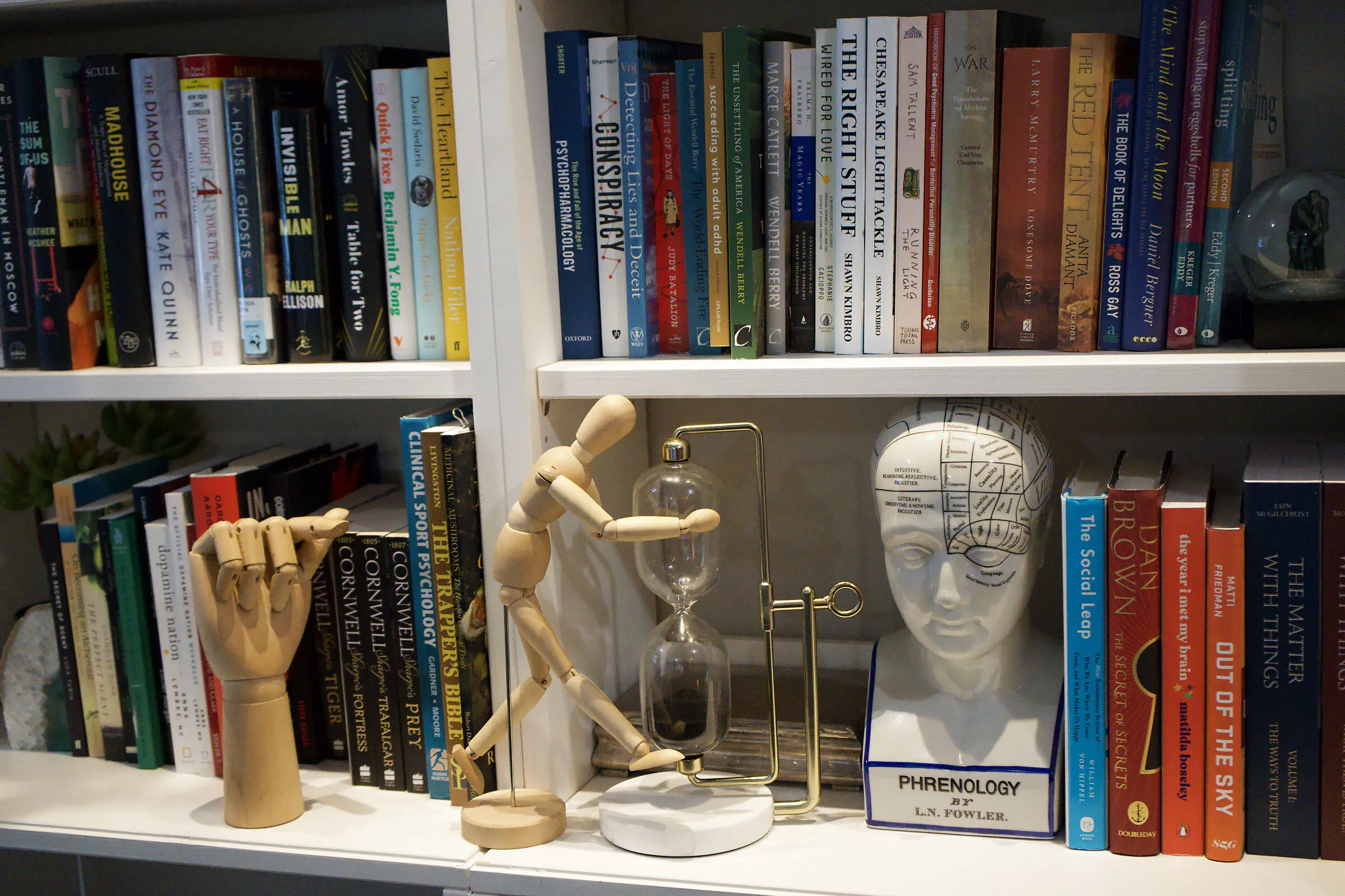 A shelf in Dr. Clements's Chadds Ford office with a phrenology head, an artist's articulated hand, an hourglass, and books on the mind
